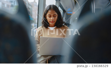 Young woman using laptop while commuting on public bus, candid real life moment with soft natural light and shallow depth of field. Modern morning routine, remote work and urban lifestyle concept 138166329