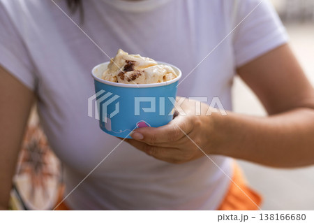 Close up of female hands holding a refreshing gelato cup against a clean white t shirt background. Minimalist summer food aesthetic with empty space on clothing for mockup Close up of female hands holding a refreshing gelato cup against a clean white t shirt background. Minimalist summer food aesthetic with empty space on clothing for mockup 138166680
