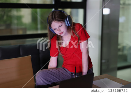 Focused girl engaged in online learning while wearing headphones in a modern workspace during the afternoon 138166722