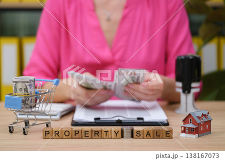 Transaction of property in an office setting with cash, documents, and a miniature house on the table, signaling a successful sale Transaction of property in an office setting with cash, documents, and a miniature house on the table, signaling a successful sale 138167073