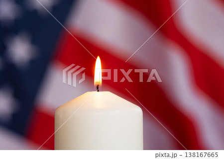 Lit candle with flame against blurred USA flag background, symbol of remembrance, patriotism and unity Lit candle with flame against blurred USA flag background, symbol of remembrance, patriotism and unity 138167665