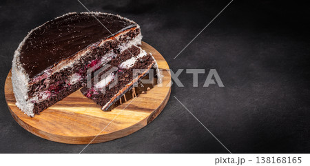 Chocolate cake with sliced piece on wooden board over dark background 138168165