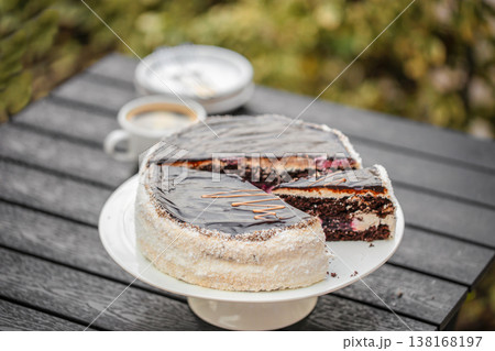 Chocolate cake with slice on stand and coffee on outdoor table Chocolate cake with slice on stand and coffee on outdoor table 138168197