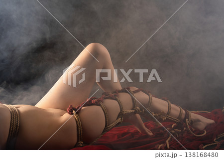 Sensual cropped view of a body bound in artistic Shibari ropes lying on red fabric Sensual cropped view of a body bound in artistic Shibari ropes lying on red fabric 138168480