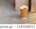 Black tea takeaway. Paper cup with tea bag on a wooden background. Breakfast break.  One-use drinkware. 138168651