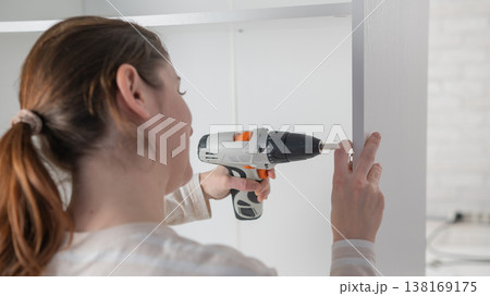 A Caucasian woman uses a screwdriver to tighten a screw while assembling a cabinet. 138169175