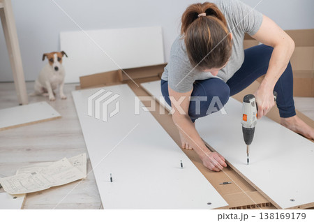 A Caucasian woman uses a screwdriver to tighten a screw while assembling a cabinet. 138169179