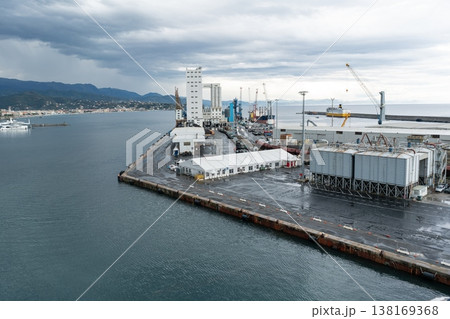 Industrial pier with silos warehouses and coastal mountains. Savona, Italy Industrial pier with silos warehouses and coastal mountains. Savona, Italy 138169368