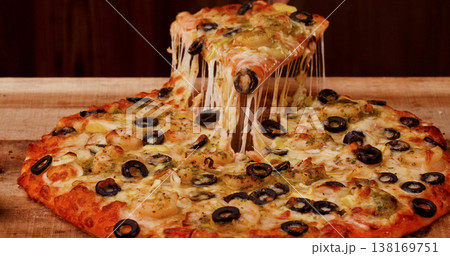 Delicious cheese pizza with olives being served on a wooden table at a local restaurant during the evening Delicious cheese pizza with olives being served on a wooden table at a local restaurant during the evening 138169751