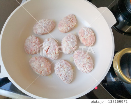 Raw breaded meat cutlets or patties arranged in a white frying pan with oil, ready to be cooked Raw breaded meat cutlets or patties arranged in a white frying pan with oil, ready to be cooked 138169971