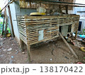 Rustic wooden chicken coop stands outdoors. Pallets form sturdy, weathered walls and floor. Small doorway offers shelter for poultry. Roof shelters birds from rain and sun. Dirt ground shows rural 138170422