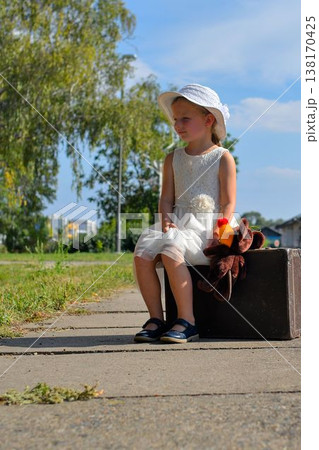 A sweet little girl at the train station. A cute girl at the train station. A small girl holds a cuddly toy and sits on an old luggage trunk. The concept of travel, vacations, and a carefree A sweet little girl at the train station. A cute girl at the train station. A small girl holds a cuddly toy and sits on an old luggage trunk. The concept of travel, vacations, and a carefree 138170425