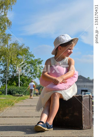 A cute girl at the train station. A little girl holds a plush toy and sits on an old suitcase. The concept of travel, vacations, and a carefree childhood. Retro and vintage vibes. A cute girl at the train station. A little girl holds a plush toy and sits on an old suitcase. The concept of travel, vacations, and a carefree childhood. Retro and vintage vibes. 138170431
