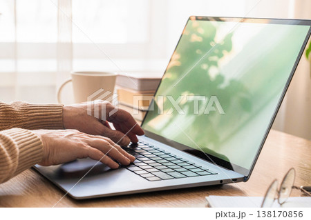 Womens hands typing on laptop keyboard, working remotely from home office desk with mug and glasses. Person typing on laptop working from home 138170856