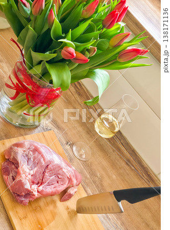 Red tulips in a basket and a piece of pork on a cutting board in close-up. Preparing for the holiday, making festive dishes. High quality photo Red tulips in a basket and a piece of pork on a cutting board in close-up. Preparing for the holiday, making festive dishes. High quality photo 138171136