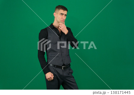 Man Thinking with Smartphone. A man in a green shirt holds a smartphone and looks up thoughtfully, against a light gray background Man Thinking with Smartphone. A man in a green shirt holds a smartphone and looks up thoughtfully, against a light gray background 138171445