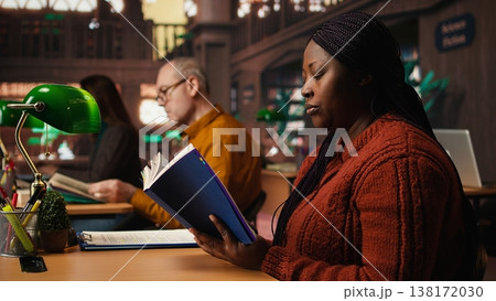 Focused woman in a study area reading and researching for master degree, reflecting the determined lifestyle of a student reaching academic and personal goals. Knowledge. 138172030