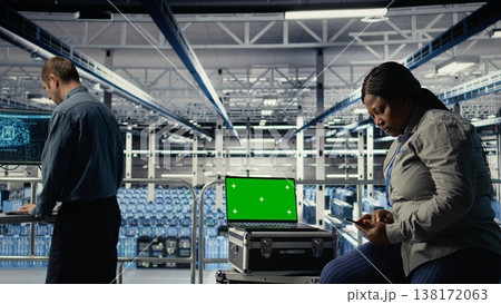 IT coworkers monitors server farm activity using isolated screen laptop. Data center engineers review rigs tests results on chroma key notebook to ensure systems are working correctly, camera A 138172063