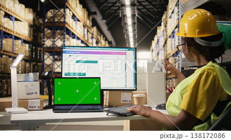 Stock room employee looks at phone with copy space and follows parcels on pc software, handling import export operations for e-commerce large business. Order fulfillment in depot. Camera A. 138172086