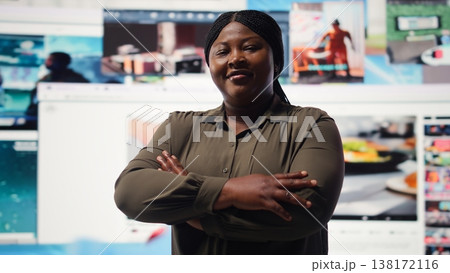 Portrait of cheerful woman celebrating freedom of unlimited video content in metaverse. Happy person stands with crossed arms in front of giant digital wall with online video channels, camera A 138172116