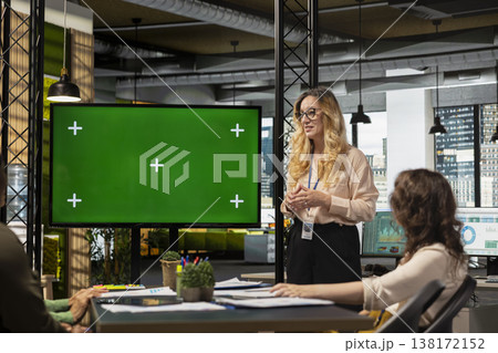 Team of businesswomen creates a strategy next to chroma key display with big TV monitor open and planning documents on the table. Associates showcasing business operations efficiency. 138172152