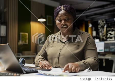 Black person making financial predictions with data insights on laptop, doing overtime at midnight in the office. Woman summarizing numbers for projections and organizing a report. Black person making financial predictions with data insights on laptop, doing overtime at midnight in the office. Woman summarizing numbers for projections and organizing a report. 138172155