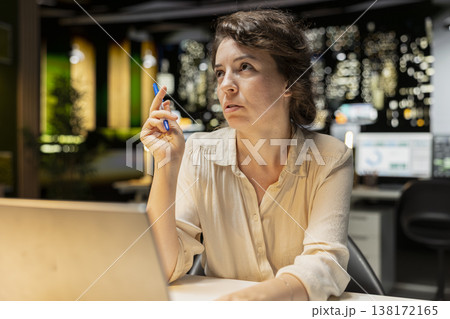 Businesswoman contemplating on complex problem in dark office late at night, strategizing and typing options on laptop. Seeking a logical solution through methodical concentration. Businesswoman contemplating on complex problem in dark office late at night, strategizing and typing options on laptop. Seeking a logical solution through methodical concentration. 138172165