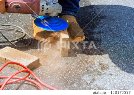 Worker cuts brick with power tool while dust flies worksite during renovation patio 138173557