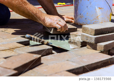 Contactor places bricks while working on patio, tools, materials are nearby, in residential setting. Contactor places bricks while working on patio, tools, materials are nearby, in residential setting. 138173560