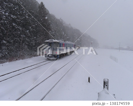 雪が舞い散る中を走るローカル線 138174559