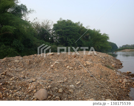 Gravel riverbank river stone sand nature outdoor landscape forest green water Gravel riverbank with stone and sand beside calm river, lush green forest vegetation riverside soft sky creating 138175539