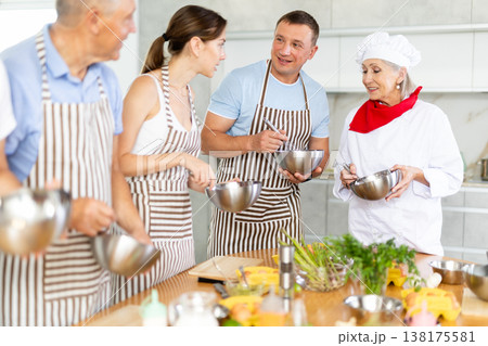 Smiling old woman chef of cooking course teaching attendees how to mix sauce Smiling old woman chef of cooking course teaching attendees how to mix sauce 138175581