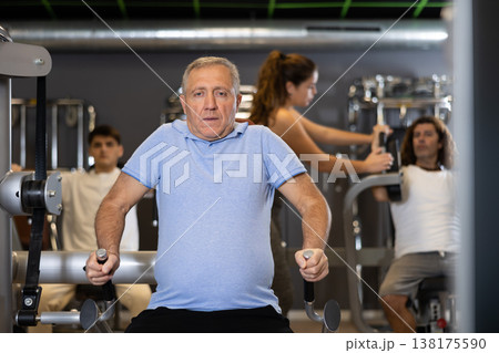 Elderly active man exercising on a simulator in modern gym 138175590