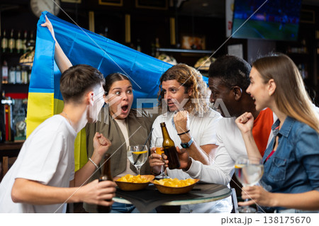 Emotional people waving flag of Ukraine while watching football match in sports pub Emotional people waving flag of Ukraine while watching football match in sports pub 138175670