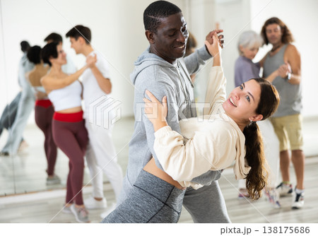 Happy african-american guy and caucasian girl practising paired latin dance in dance studio Happy african-american guy and caucasian girl practising paired latin dance in dance studio 138175686