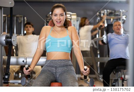 Young girl performing triceps press in exercise machine in gym 138175702