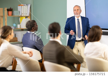 Senior man lecturer with remote controller speaks to business audience of listeners Senior man lecturer with remote controller speaks to business audience of listeners 138175721