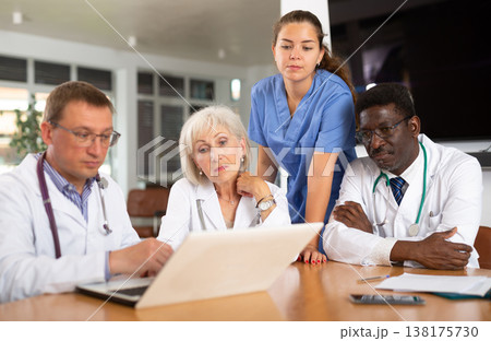 Doctors sitting around the table looking at the notebook Doctors sitting around the table looking at the notebook 138175730
