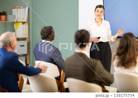 Woman lecturer with remote controller speaks to business audience of listeners, Woman lecturer with remote controller speaks to business audience of listeners, 138175754