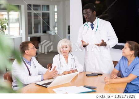 Middle-aged doctor talking to his colleagues sitting around table 138175829