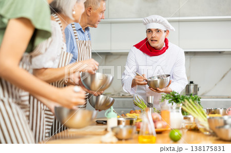 Young guy cook teaches to cook group of people Young guy cook teaches to cook group of people 138175831