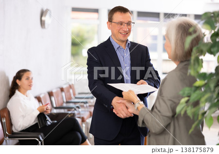 Middle-aged man handshaking with other person in waiting room Middle-aged man handshaking with other person in waiting room 138175879