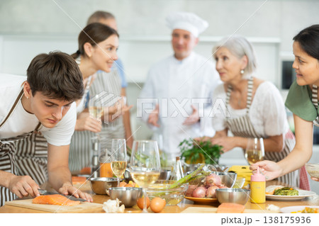Pleased young man learner of culinary classes cutting piece of salmon Pleased young man learner of culinary classes cutting piece of salmon 138175936