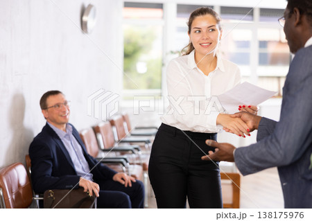 Woman makes deal, shaking hands with middle-aged African man colleague while standing in office 138175976
