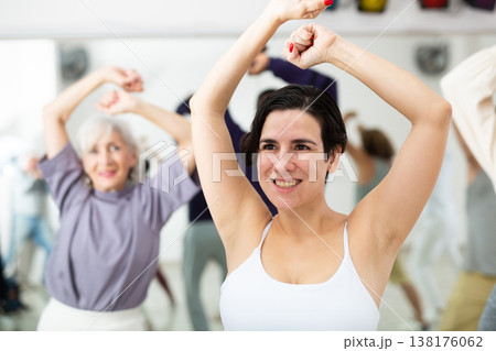 Happy young woman practising modern dance moves with other people in dance studio 138176062