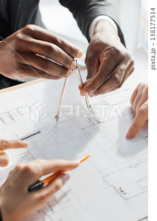 Hands using a compass and pens to mark detailed architectural plans during a collaborative design meeting 138177514
