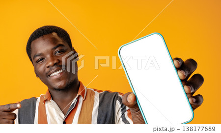 Person shows smartphone with empty screen against yellow background in studio setting 138177689