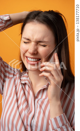 Young woman talks on phone with a frustrated expression against a bright orange background 138177710