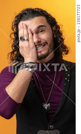 Man with curly hair covers one eye and smiles against a yellow background 138177723