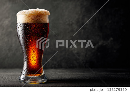 A glass of dark beer with rich foam shown on a dark background, concept of refreshment and craft brewing A glass of dark beer with rich foam shown on a dark background, concept of refreshment and craft brewing 138179530